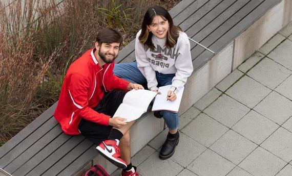 两个体育博彩app的学生坐在外面的长凳上，微笑着看着镜头