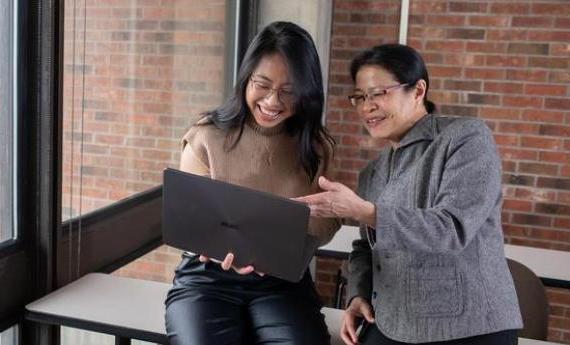 一位体育博彩app的学生和她的导师一起看着一台笔记本电脑，面带微笑