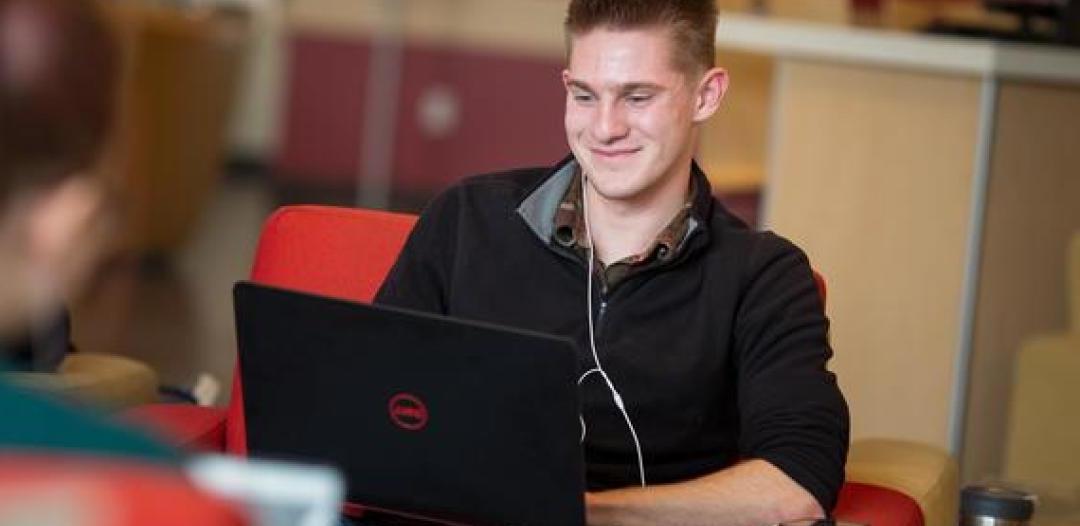 一位体育博彩app的学生坐在那里，膝上放着一台笔记本电脑，微笑着打字