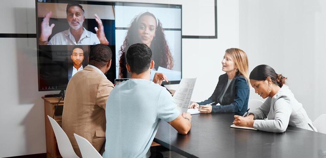 一群人坐在一张桌子前，在大屏幕上进行视频会议