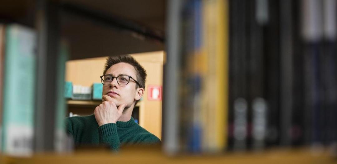 一个人戴着眼镜，用手托着下巴凝视着图书馆的书架